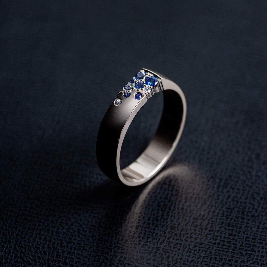 5mm wide Kero ring in 18K white gold with multiple blue sapphires photographed on a dark background. Design by Jussi Louesalmi, Au3 Goldsmiths.