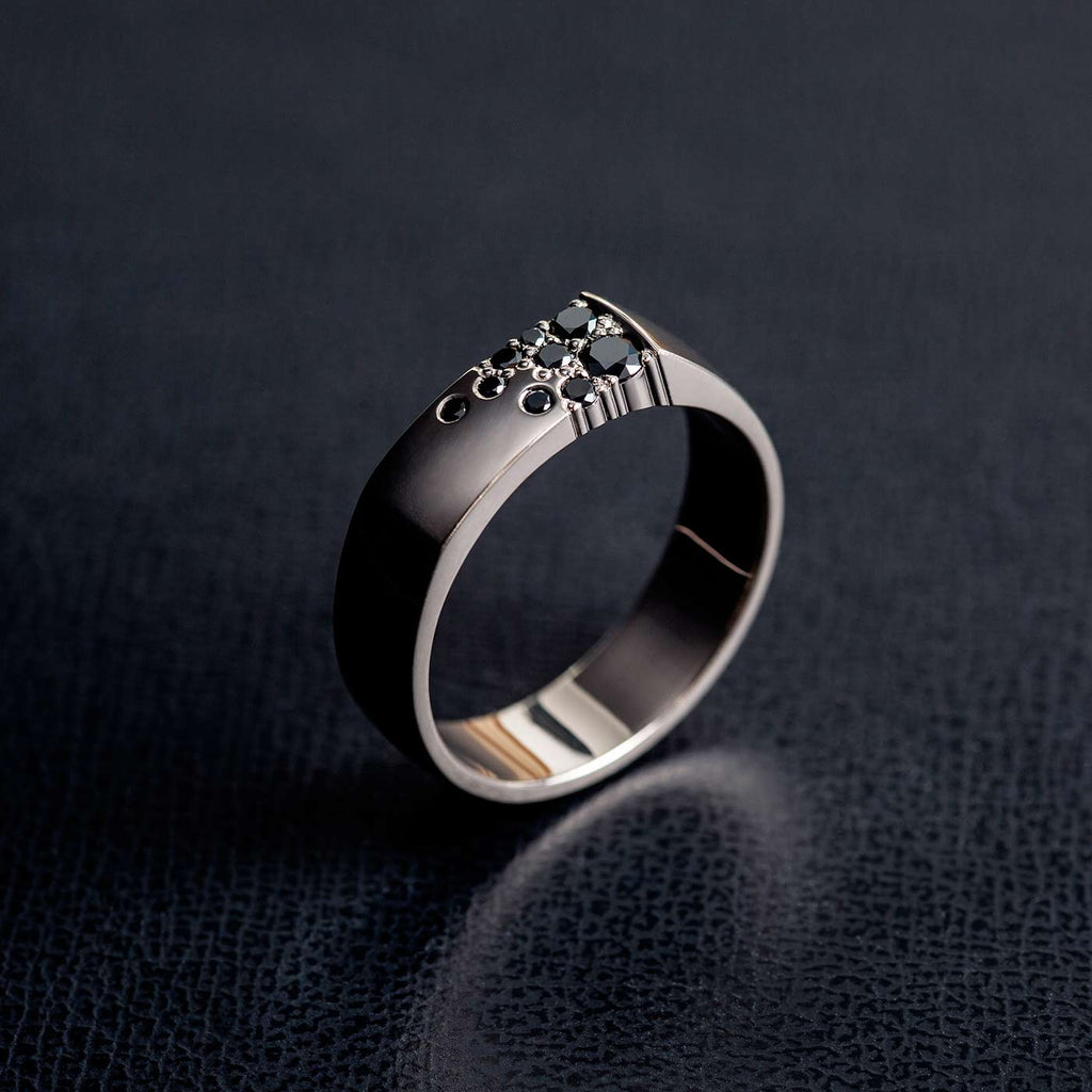 6mm wide Kero ring in 18K white gold with multiple black diamonds photographed on a dark background. Design by Jussi Louesalmi, Au3 Goldsmiths.