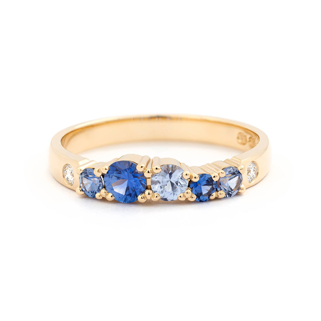 Different size blue sapphires and small white diamonds in a Keto Meado 2,5mm wide row ring made in 18K yellow gold. Design by Jussi Louesalmi, Au3 Goldsmiths.