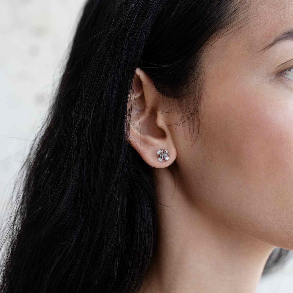 A dark haired model wearing wavy Dione stud earrings, design Anu Kaartinen, Au3 Goldsmiths
