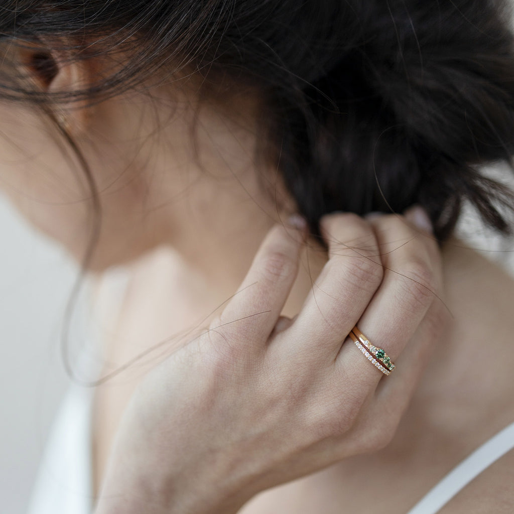 Dark haired model has 2mm wide Keto Meadow ring with green and white diamonds and 1,5 mm wide Raita ring with white diamonds on her finger, both rings are made in 750 gold. Design by Jussi Louesalmi, Au3 Goldsmiths.
