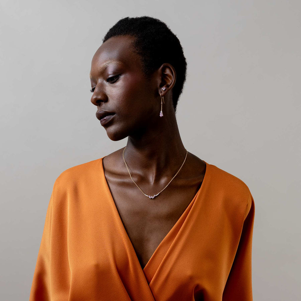 Model wearing an orange jumpsuit and a Keto Meadow necklace and earrings with colorful sapphires and white diamonds. Design by Jussi Louesalmi, Au3 Goldsmiths.
