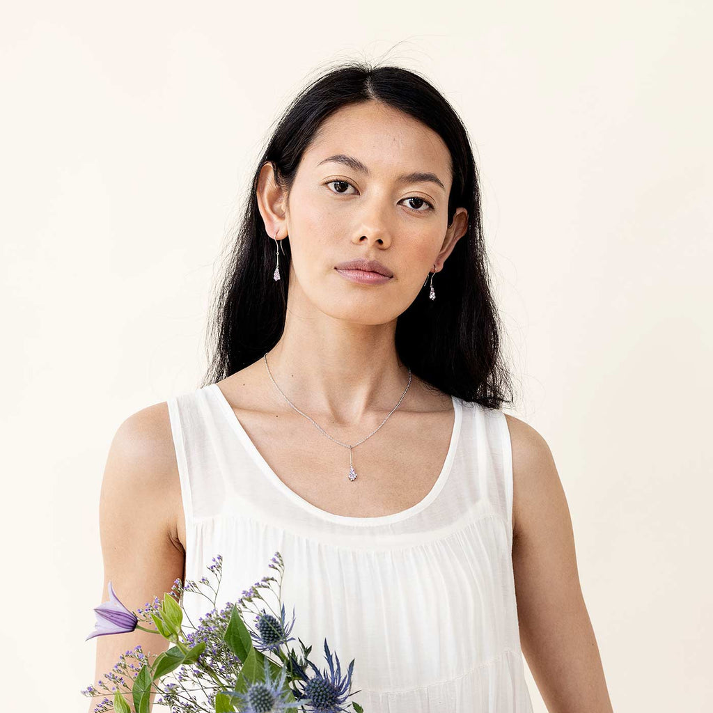 A dark haired model wearing hanging Keto Meadow earrings and a pendant. Design by Jussi Louesalmi, Au3 Goldsmiths.