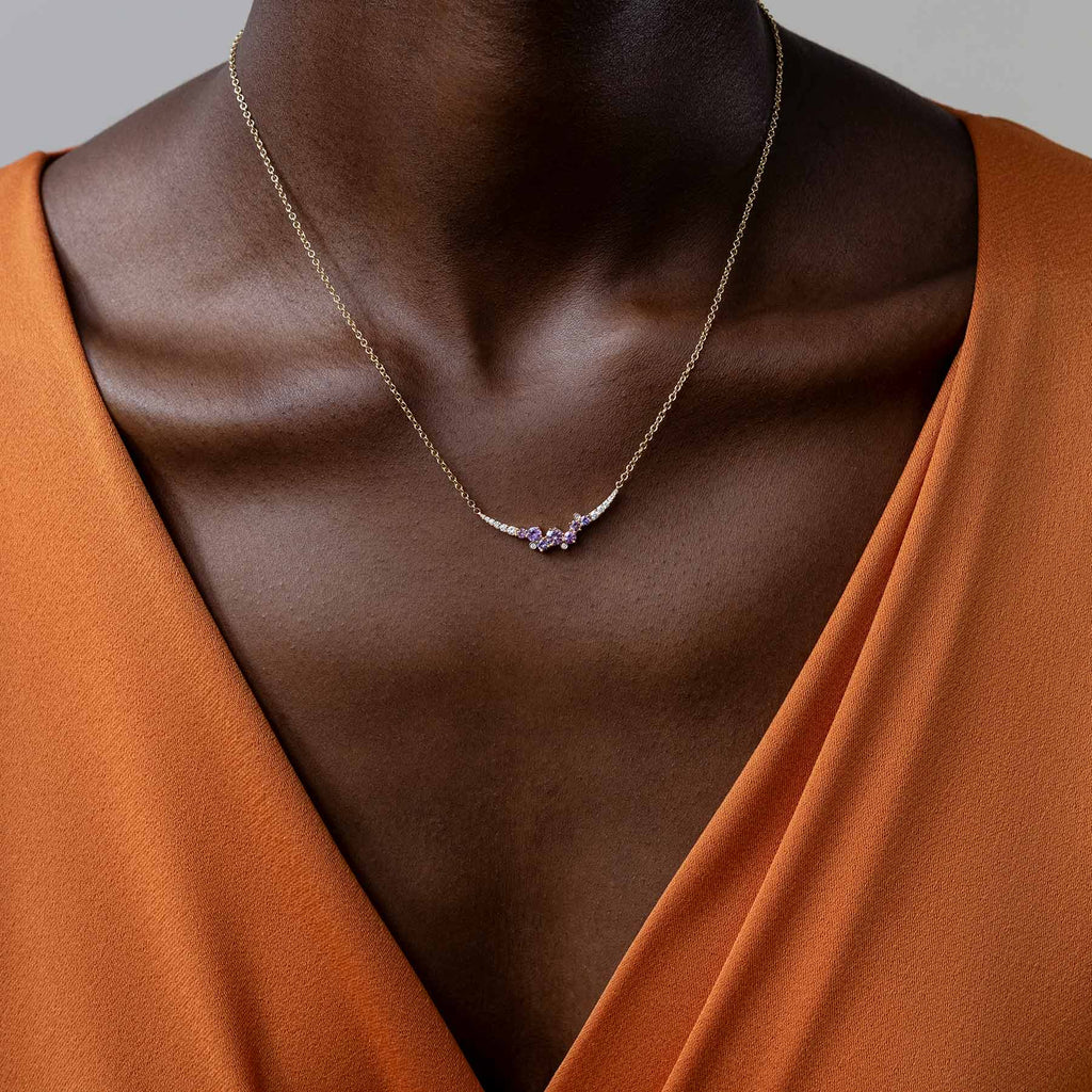 Model wearing an orange jumpsuit and a Keto Meadow necklace with colorful sapphires and white diamonds. Design by Jussi Louesalmi, Au3 Goldsmiths.